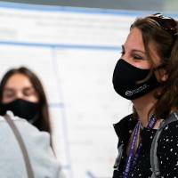 Mentor wearing mask listening to scholar's poster presentation.